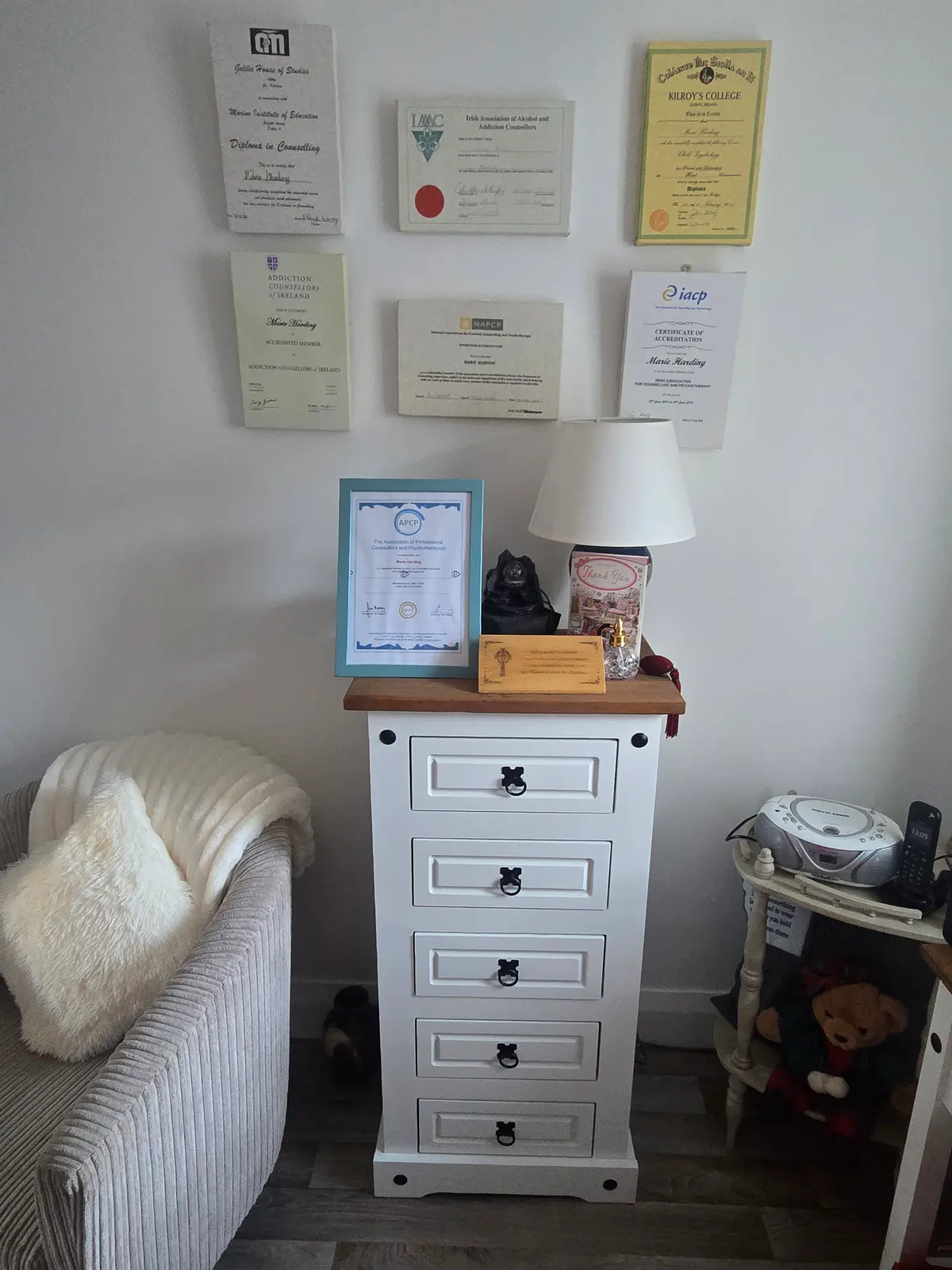 A wide view of the counselling room showing the seating area, a lamp, and certificates displayed on the wall.